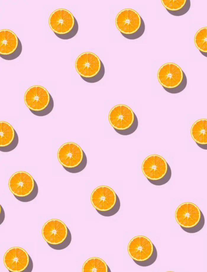 A seamless pattern of fresh orange halves on a pastel pink background, casting soft shadows.