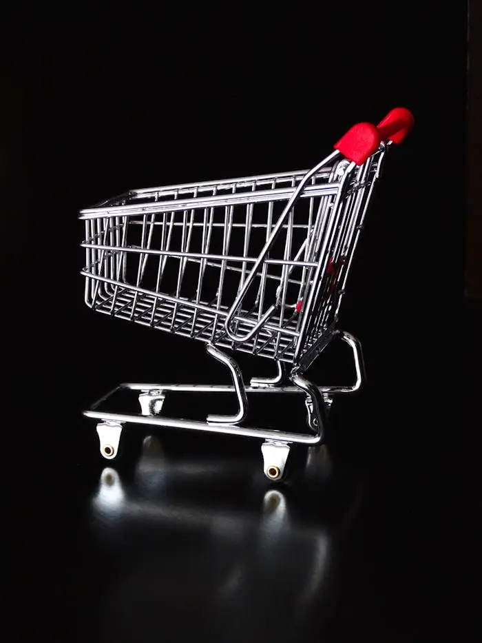 A shiny miniature shopping cart with red handles on a black reflective surface.